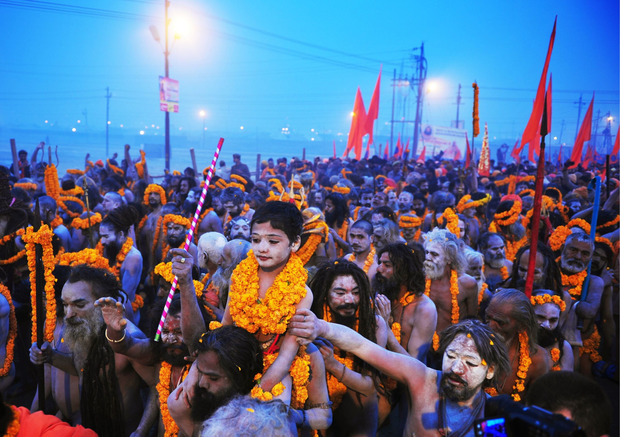 TO GO WITH AFP STORY BY ADAM PLOWRIGHT - Sadhus or holy men (L) carry a child adorned with marigold flowers on their shoulders as they all march towards the Sangham or the confluence of the the Yamuna and Ganges rivers during the Kumbh Mela in Allahabad on January 14, 2013. Hundreds of thousands of Hindu pilgrims led by naked, ash-covered holy men streamed into the sacred river Ganges on Monday at the start of the world's biggest religious festival. The Kumbh Mela in the Indian town of Allahabad will see up to 100 million worshippers gather over the next 55 days to take a ritual bath in the holy waters, believed to cleanse sins and bestow blessings. Before daybreak on Monday, a day chosen by astrologers as auspicious, hundreds of gurus, some brandishing swords and tridents, ran into the swirling and freezing waters for the first bath, signalling the start of events.AFP PHOTO/SANJAY KANOJIA